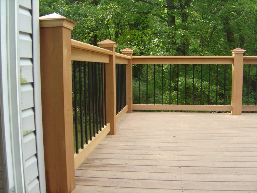 Wooden deck with black metal railing and green foliage in the background.
