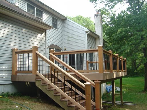 Wooden deck with stairs and railing attached to a house, surrounded by trees.