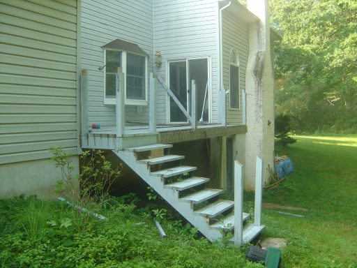 Exterior staircase leading to a deck, surrounded by greenery and a home wall.