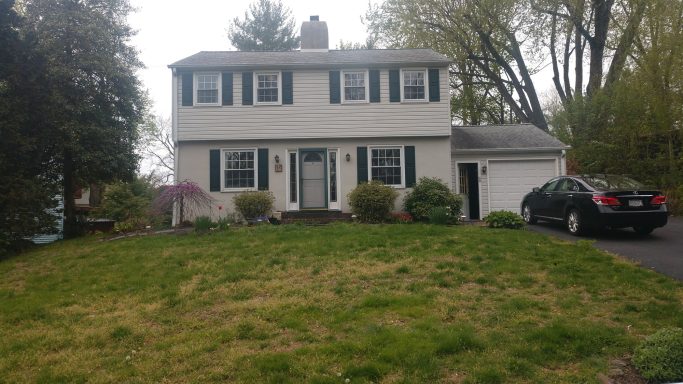 Two-story white house with a black car parked beside it and greenery in the front yard.