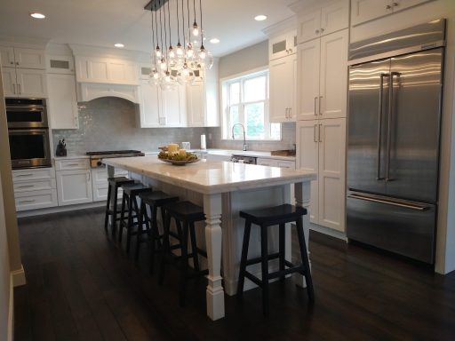 Modern kitchen with white cabinets, large island, and dark wood flooring.