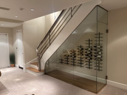 Modern interior featuring a glass wine rack beneath a staircase.
