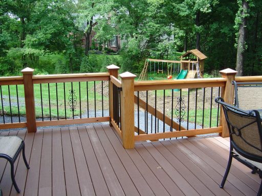 Wooden deck with railing, overlooking a grassy yard and playset in the background.