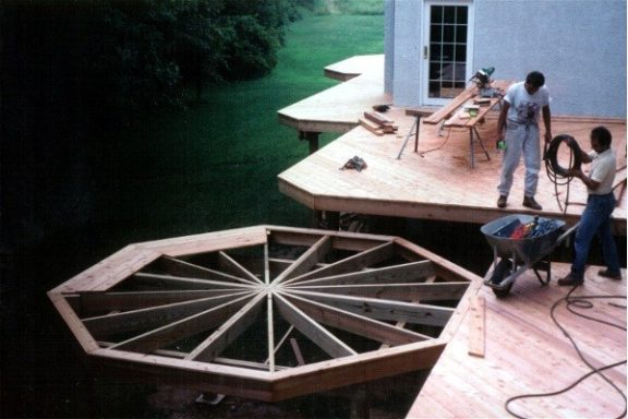 Construction workers building a circular wooden deck on a home.