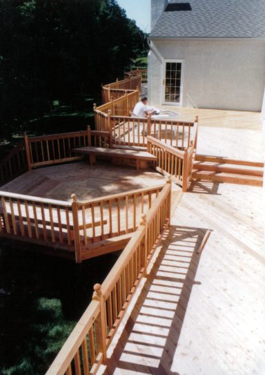 A spacious wooden deck with multiple levels and railings, surrounded by greenery.