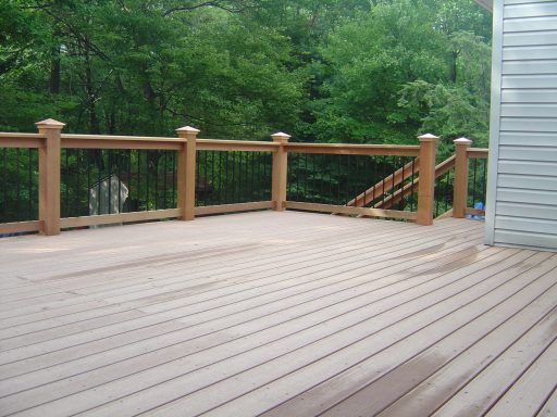 Wooden deck with railing, surrounded by greenery and a residential building.
