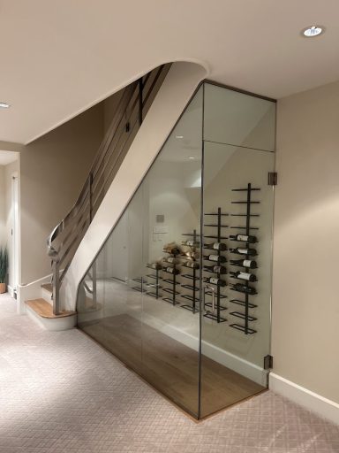 Glass wine cellar under a staircase with a wooden base and a modern railing.