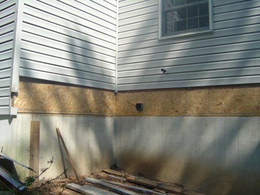 Corner of a house showing wood siding, exposed wall, and construction materials.