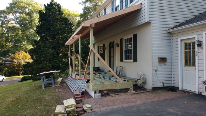 Construction of a new porch on a house, with scaffolding and building materials nearby.