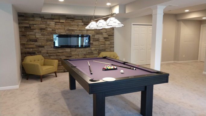 A game room featuring a purple pool table, stone wall, and modern lighting.