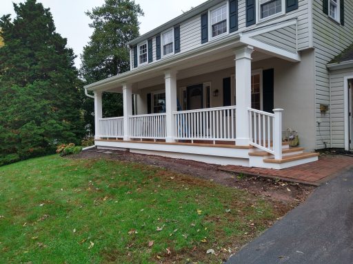 Front view of a house with a porch, white railings, and a well-maintained lawn.