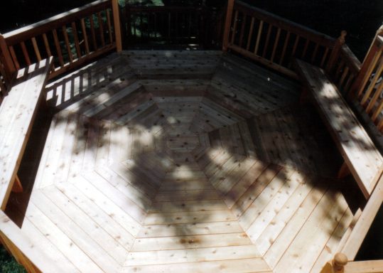 Wooden octagonal deck with surrounding railings, sunlight creating shadow patterns.