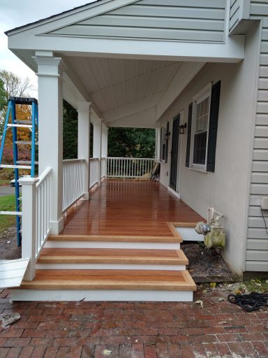 Newly finished wooden porch with steps and railing beside a house.